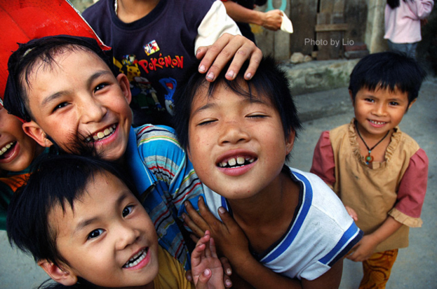 Kinder, die lachend vor einer Straße und einer Wand stehen.