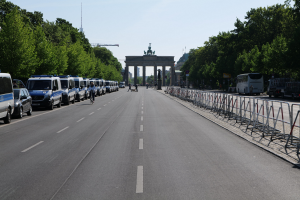 Lange Reihe von Polizeiwagen auf der Straße vor dem Brandenburger Tor in Berlin, Deutschland, mit Menschen auf Fahrrädern und Barrikaden auf der Straße, Bäumen an den Seiten und einem Tor mit Statuen im Hintergrund.
