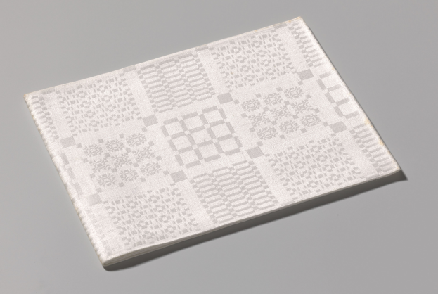 Ein weißes Buch mit einem QR-Code auf dem Cover liegt auf einer grauen Oberfläche.