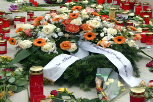 Mahnmal in Berlin mit Blumen und Kerzen auf dem Boden vor einer Wand.