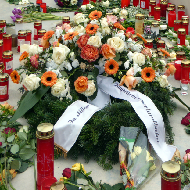 Mahnmal in Berlin mit Blumen und Kerzen auf dem Boden vor einer Wand.