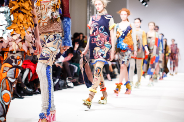 Eine Gruppe Von Frauen, Die Auf Einem Laufsteg In London Fashion Week Gehen, Mit Einer Zuschauerschaft Im Hintergrund Unter Hellen Lichtern.
