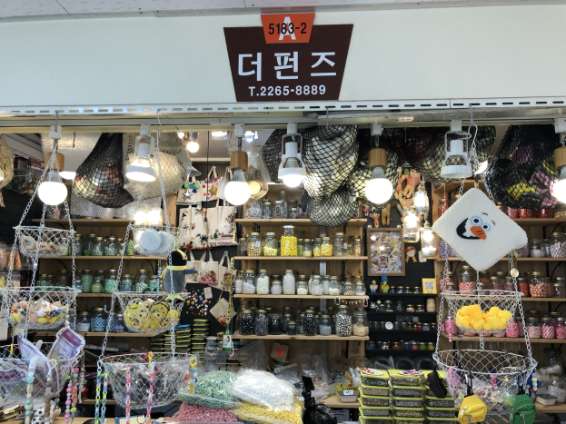 Ein unordentlicher Laden in Seoul, der verschiedene Gegenstände wie Körbe, Lichter, Flaschen und Spielzeuge auf Regalen ausstellt, mit einer Tafel öber der Tür, die anzeigt, dass es einer der besten koreanischen Läden ist.