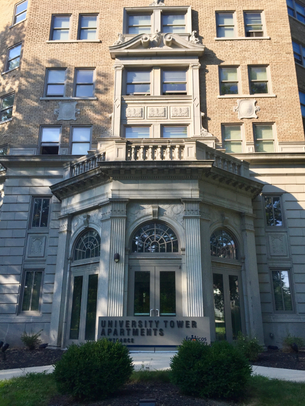 Die University Tower Apartments in Chicago, Illinois, ein großes Gebäude mit Glasfenstern und -türen, umgeben von saftigem Grün und Pflanzen, mit einer Tafel mit Text davor und dem Himmel im Hintergrund.