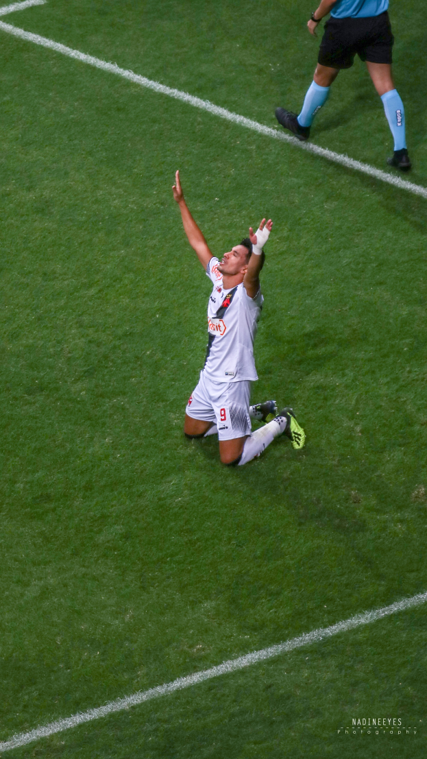 Ein Fußballspieler kniet auf dem Boden mit ausgestreckten Armen in Feierlaune, trägt eine Sportuniform und Schuhe.