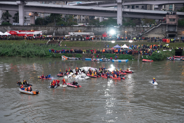 Eine Gruppe von Menschen in kleinen Booten auf einem Gewässer, umgeben von Vegetation und Infrastruktur, tragen Rettungswesten während einer Rettungsaktion.