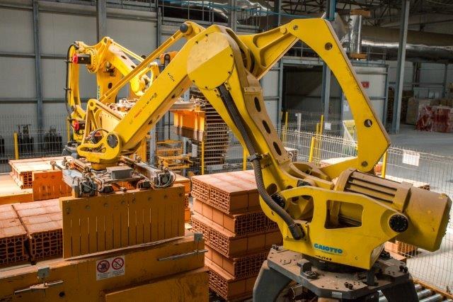 Großes industrielles Lager mit gestapelten Kisten, Überdachkränen, Zaun, Pfählen und einer fernen Wand in einer automatisierten Manufacturing-Umgebung.