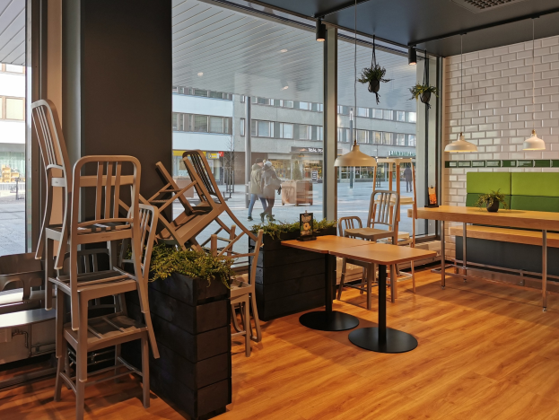 Ein Restaurantinnenraum mit Holztischen und -stühlen, die durch ein großes Fenster sichtbar sind, das eine städtische Außenansicht in Berlin, Deutschland, zeigt.