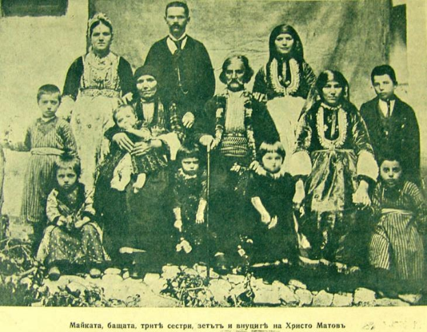 Schwarz-weiß-Foto einer Familie, die vor einer Vorhangwand posiert, beschriftet mit 'Russische Familie um 1900'.