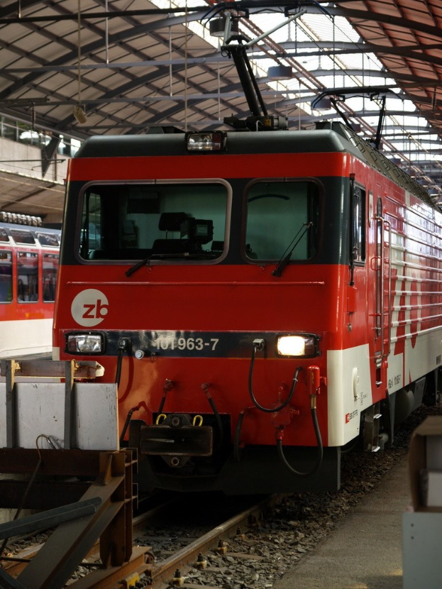 Ein Zug fährt auf einem Gleis mit Steinen und Stäben in der Nähe, mit Text auf der Seite.