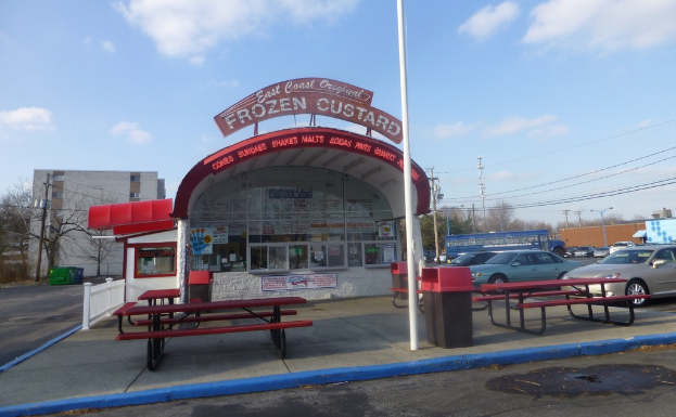 Ein Parkplatz mit Autos, Pfählen, Gebäuden, Bänken, einem Schuppen mit einer Tafel und Plakaten auf dem Schuppen.