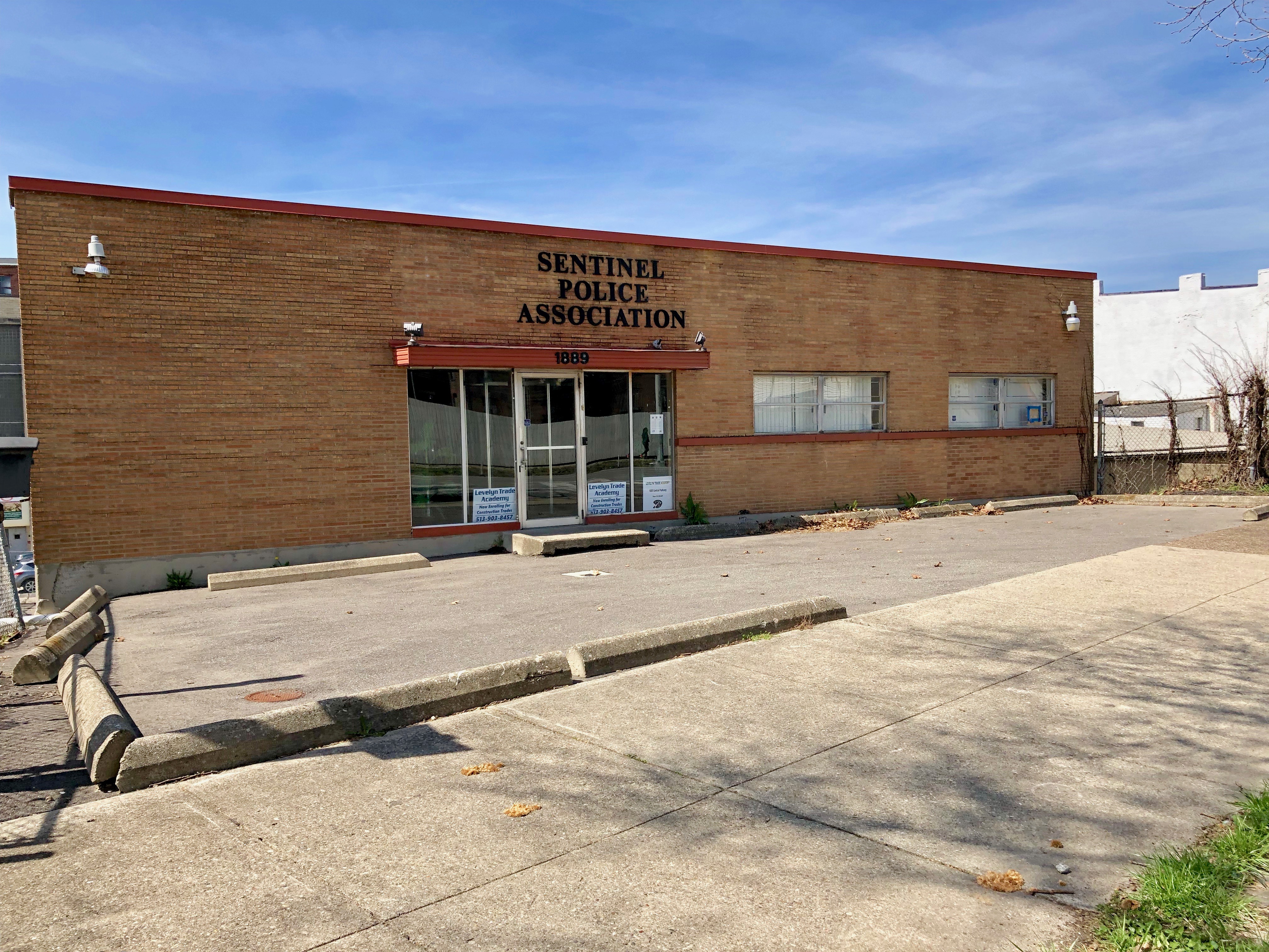 Das Sentinel Police Association Building in Detroit, Michigan, ein braunes Gebäude mit Glasfenstern und -türen, hat Text an seiner Wand, mit einem Baum rechts daneben und einem klaren blauen Himmel im Hintergrund.