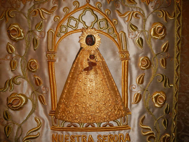 Goldene Stickerei mit einer friedlichen Frau in einem hochgeschlossenen, langärmligen Kleid mit einem Dutt, umgeben von detaillierten Texten und prächtigen goldenen Designs.