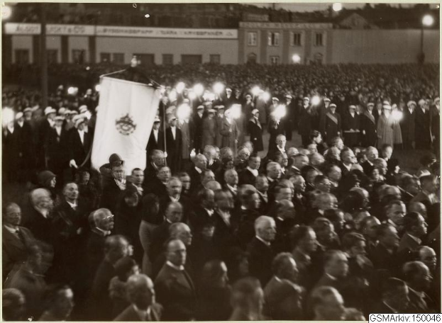 Schwarzes und weißes Foto einer großen Menge vor einem Gebäude, mit einer Person, die eine Fahne hält, Polen und Lichter im Hintergrund und Text unten, der "Gustav Klimts Rede an der Berliner Mauer" lautet.