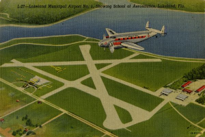 Luftaufnahme des Lakeland Municipal Airport mit einem Flugzeug, das über die Start- und Landebahn fliegt, umgeben von Bäumen, Gebäuden und Wasser, mit Text oben auf dem Bild.