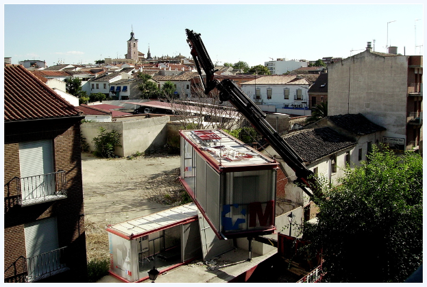 Eine Stadtansicht mit zahlreichen Gebäuden, Bäumen und einem Kran, der einen Container hält.