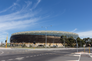 Ein großes Stadion mit starkem Verkehr davor, umgeben von Straßenlaternen, Lichtern, Ampeln, Schildern, Geländern, Bäumen und einem bewölkten Himmel.