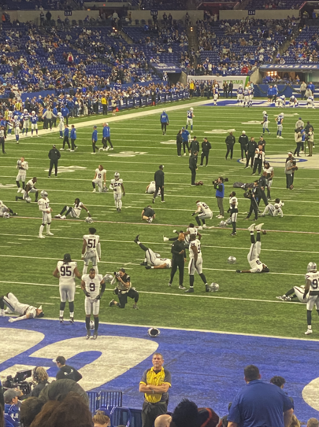 Ein Fußballspiel wird in einem Stadion mit Zuschauern, die stehen und einige sitzen, sowie einer Person mit einer Kamera, die auf eine Live-Übertragung hinweist, gespielt.