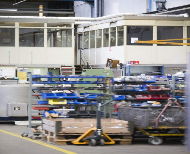 Großes Lagerinnere mit verschiedenen Geräten einschließlich fahrbaren Wagen, Schränken und einer Box, mit einer Glaswand und freiliegenden Rohren im Hintergrund.