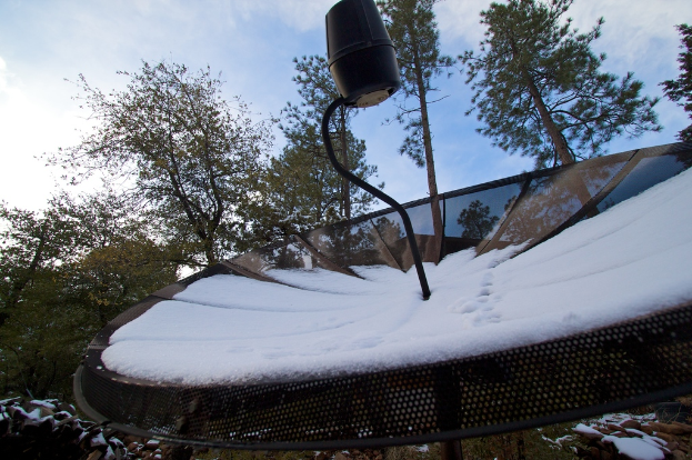 Eine Schnee bedeckte Schüsselantenne mit ein paar Bäumen und einem klaren Himmel im Hintergrund.