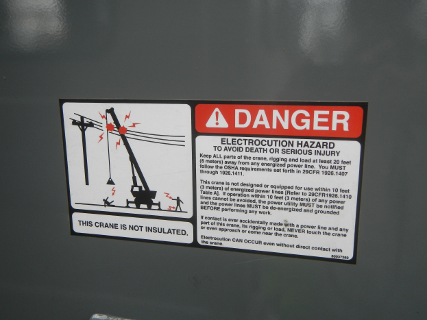 Eine Warnschild an einem Gebäude mit der Aufschrift "Gefahr" und einem Bild eines Krans im Hintergrund.