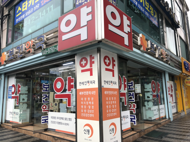 Außenansicht einer modernen Glasfassade einer Apotheke in Seoul, Südkorea, mit einem Schild und Informationsschildern, die darauf hinweisen, dass es die erste Apotheke der Stadt ist.