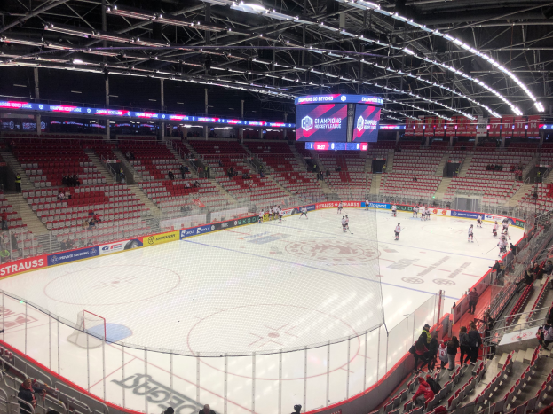 Ein Hockey-Spiel in einer großen Arena mit Zuschauern auf den Sitzen und Stehplätzen, einem Zaun um die Eisfläche, einem Bildschirm mit der Aufschrift "St. Louis Blues gegen Detroit Red Wings", Metallrahmen und einer Decke mit Deckenleuchten.