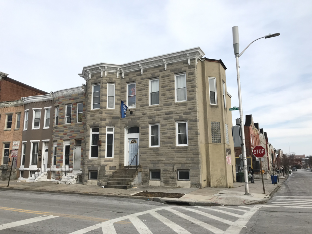 Reihe neuer Häuser an einer Straßenecke in Philadelphia mit Fahrzeugen, Bäumen und einem bewölkten Himmel im Hintergrund.