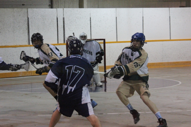 Männer in Helmen mit Stöcken scheinen in einem Innenraum mit einem Netz im Hintergrund zu kämpfen.