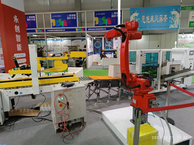 Eine Gruppe von Robotern auf einem Tisch in einer Fabrikumgebung umgeben von Maschinen, Kabeln, Leiterplatten und beleuchteten Komponenten, mit Menschen im Hintergrund.