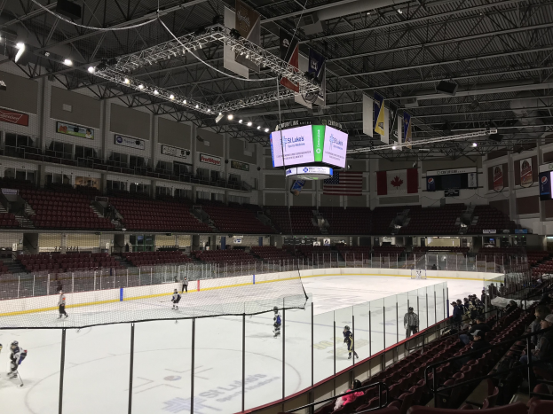 Ein Hockey-Spiel in einer großen Arena mit einem zentralen Netz, Zuschauern auf beiden Seiten und Bannern an den Wänden unter einer beleuchteten Decke.