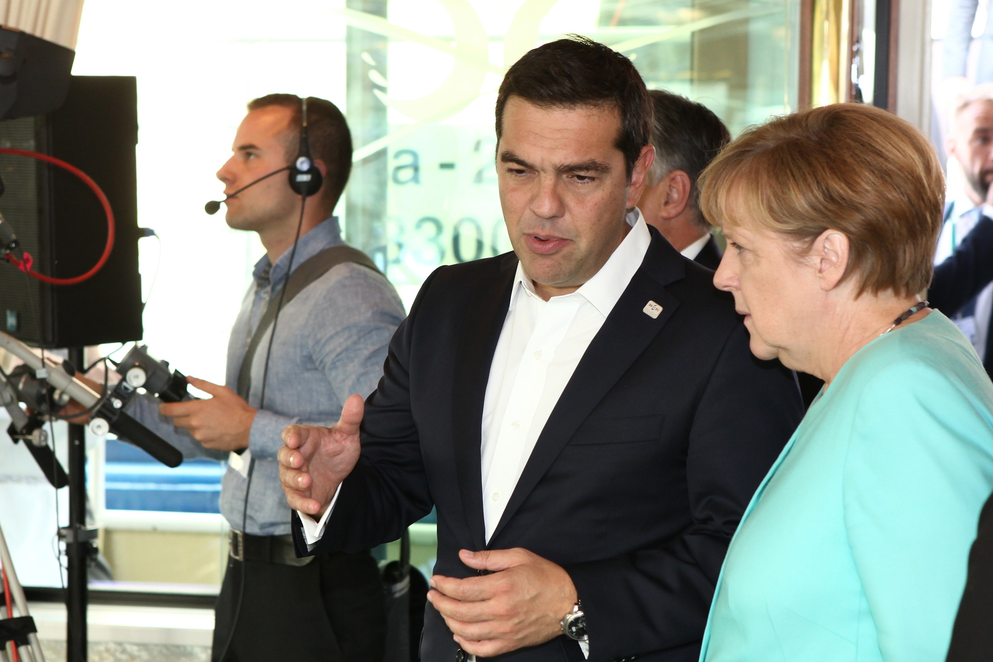 Bundeskanzlerin Angela Merkel und Bundespräsident Joachim Gauck vor einer Glaswand mit Vorhang stehend und in Mikrofone sprechend, während sie Anzüge tragen.