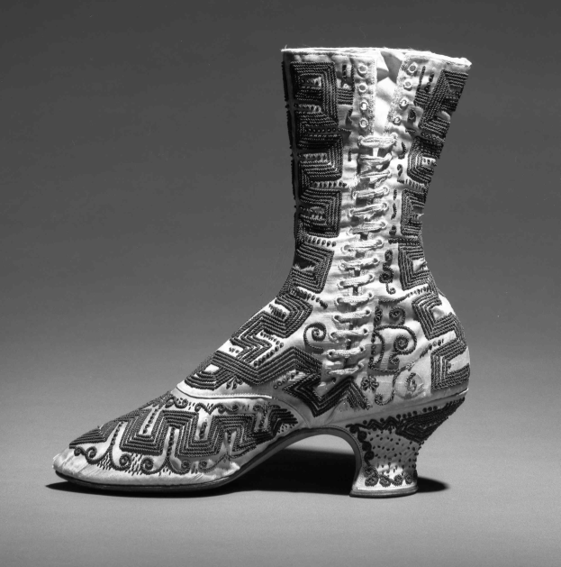 Ein Paar hochhackige Stiefel mit farbenfroher, detallierter Stickerei in Blautönen, Grüntönen und Gelb, gezeigt in Schwarz-Weiß.