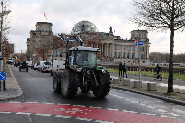 Ein grüner Traktor fährt eine Straße entlang, die von Bäumen, Laternenmasten und Schildern gesäumt ist und am Reichstaggebäude in Berlin, Deutschland, vorbeifährt, das mit Flaggen geschmückt ist.