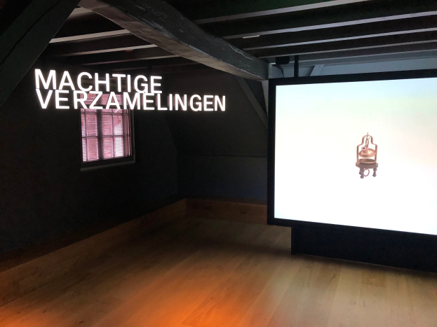 Installationsansicht der Ausstellung 'Machtige Verzamelingen' im Museum of Modern Art Berlin mit einem großen Bildschirm auf der rechten Seite und einem Fenster auf der linken Seite.