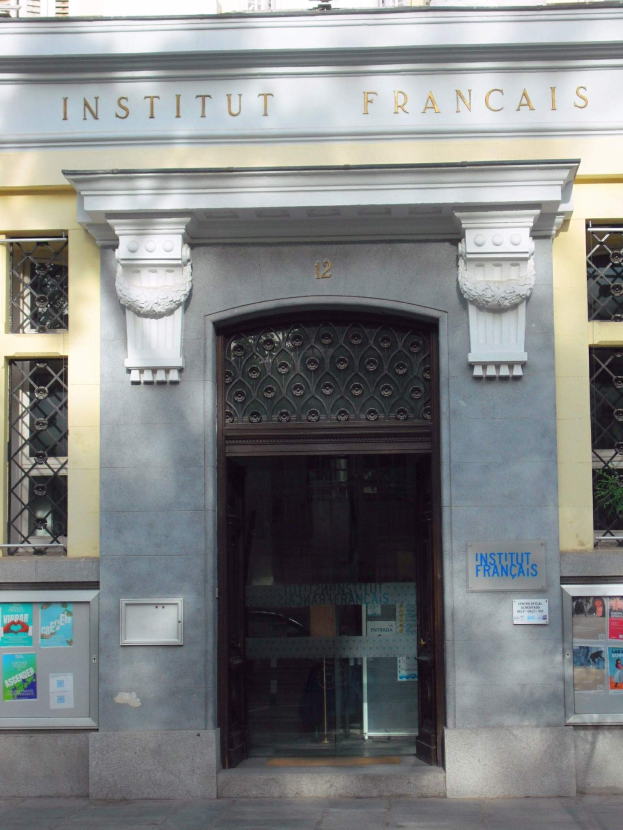 Außensicht des Institut Français in Paris, mit einem Fenster, einer Tür und Plakaten an der Wand, sowie einer Straße unten.