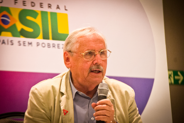 Eine Person, die in ein Mikrofon spricht und von einem Banner mit der Aufschrift 'Bundes' hinter ihr umgeben ist.