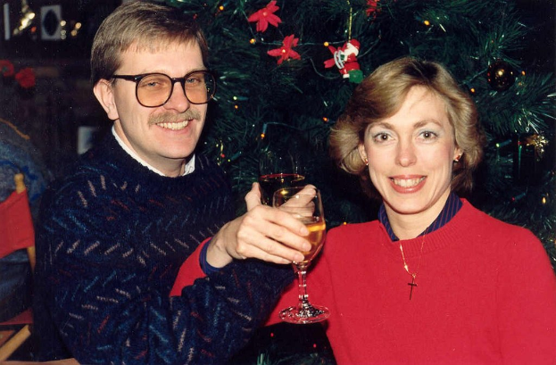 Ein Paar lächelt, während es Gläser Wein hält, mit einem Weihnachtsbaum im Hintergrund.