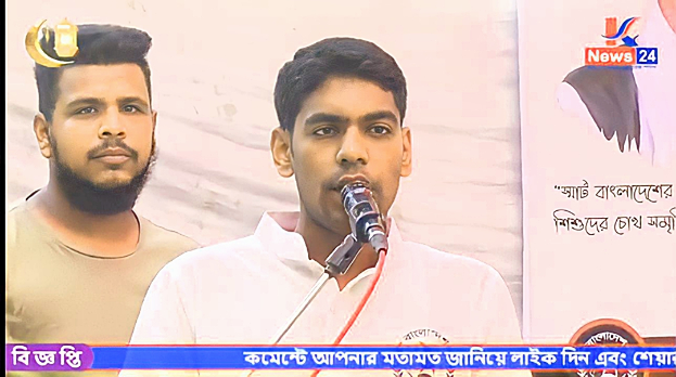 Zwei Männer stehen nebeneinander vor einem Fernseher, einer in einem weißen Hemd, der andere in einem hellgrauen T-Shirt, mit einem Banner und einem Wasserzeichen im Hintergrund.