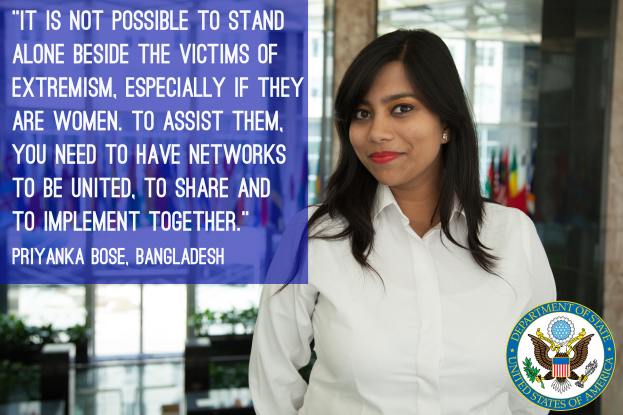 Eine Frau in einem weißen Hemd steht vor einem Gebäude mit einem Zitat über die Einheit gegen Extremismus, mit einem Logo in der rechten unteren Ecke.