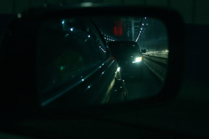 Ein Auto fährt durch einen Tunnel in der Nacht, dessen Seitenspiegel andere Fahrzeuge reflektiert, beleuchtet von Tunnel- und Autoscheinwerfern.