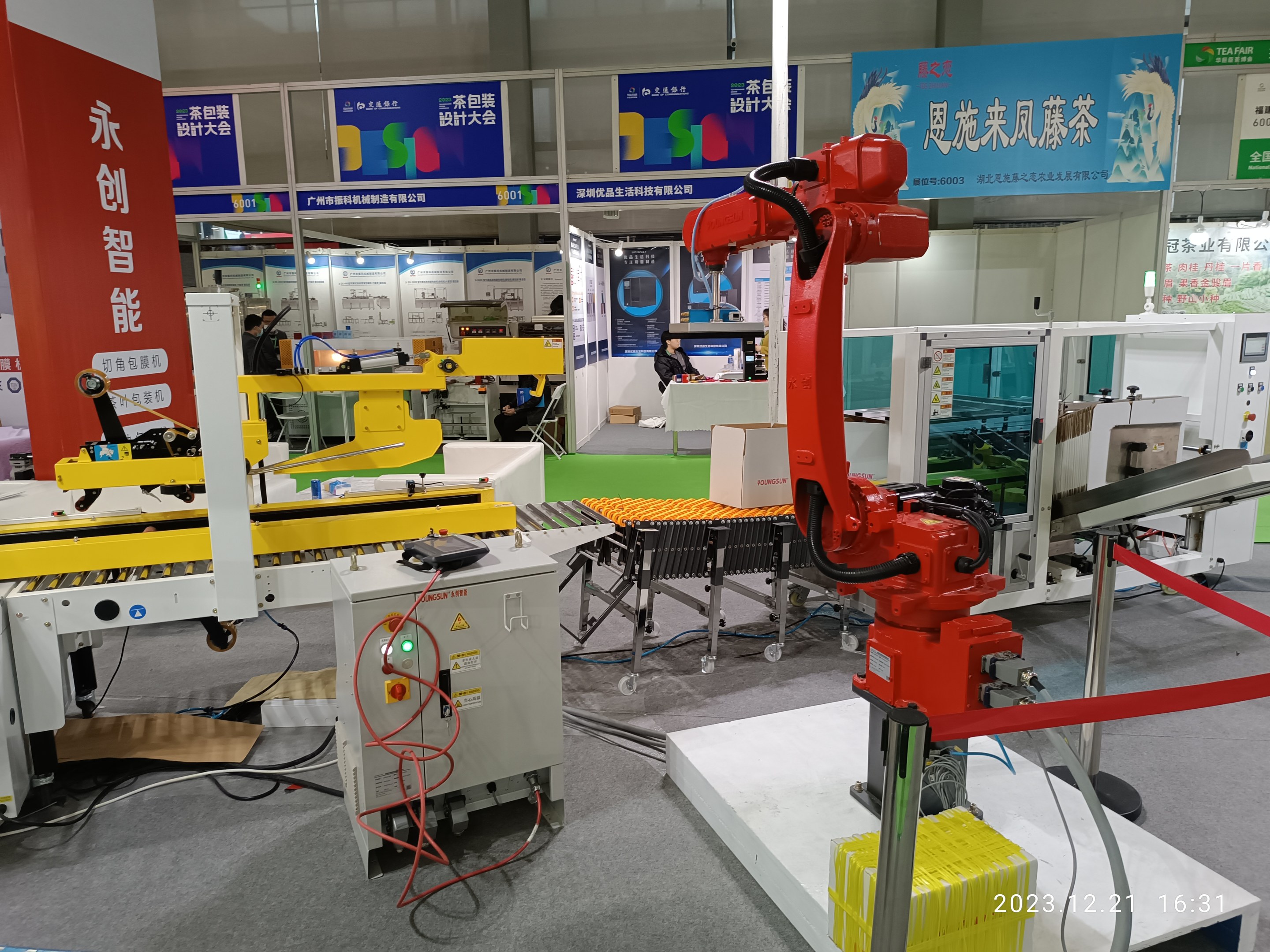 Gruppe von Robotern auf einem Tisch in einer Fabrikeinrichtung mit Maschinen, Kabeln, Text-Druckplatten, Lichtern und Menschen im Hintergrund.