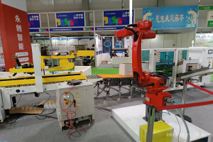 Gruppe von Robotern auf einem Tisch in einer Fabrikeinrichtung mit Maschinen, Kabeln, Text-Druckplatten, Lichtern und Menschen im Hintergrund.