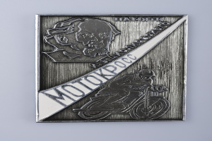 Ein Metallabzeichen mit einem Mann auf einem klassischen Motorrad vor einem hellblauen Himmel mit weißen Wolken und der Aufschrift "MOTORCYCLE".