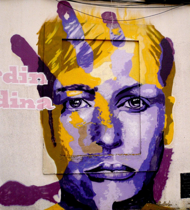 Ein lebendiges Wandgemälde eines Frauenkopfs auf einem Gebäude in Berlin, Deutschland, mit detaillierten Zügen und bunten Blautönen, Grüntönen und Gelbtönen, mit großem Text an der Wand.