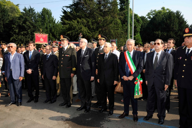 Mehrere Personen in Anzügen, die draußen mit zwei Pfählen und Bäumen im Hintergrund stehen.
