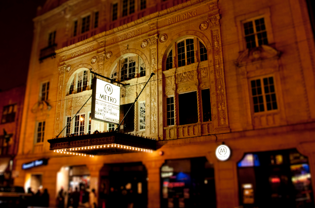 Ein gelbes Gebäude mit Geschäften im Erdgeschoss, an dem eine weiße Tafel mit der Aufschrift "Metro" hängt.