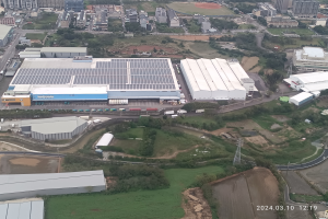 Eine Luftansicht eines großen Industriegebiets mit Gebäuden, Bäumen, Gras, Straßen, Fahrzeugen, Polen, Türmen und anderen Gegenständen, mit einem Wasserzeichen in der rechten unteren Ecke, das darauf hinweist, dass es die erste Solarstromanlage in Singapur ist.