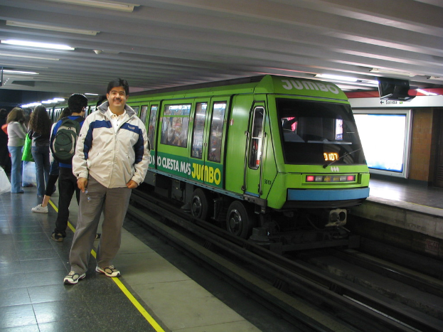 Ein Zug auf Eisenbahnschienen mit Menschen, die auf der linken Seite stehen und einem Dach oben im Bild.