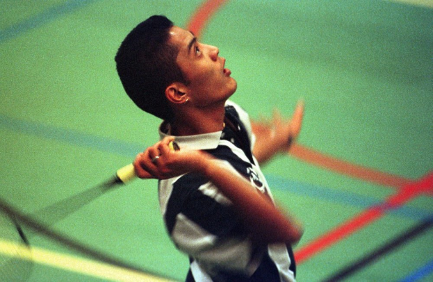 Ein junger Mann spielt Badminton auf einem Feld, hält einen Schläger und hat einen entschlossenen Gesichtsausdruck.